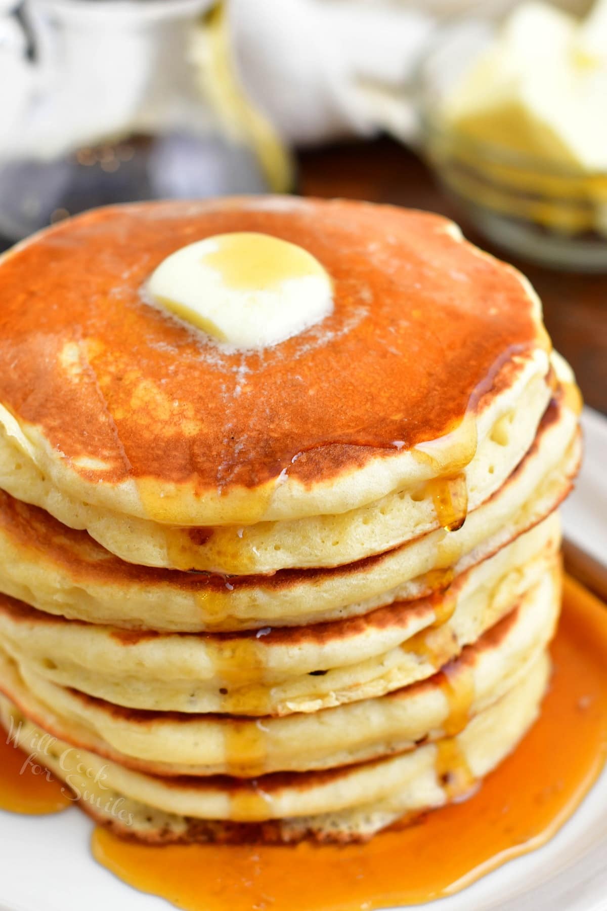 A stack of buttermilk pancakes is topped with a square of butter and drizzled with maple syrup.