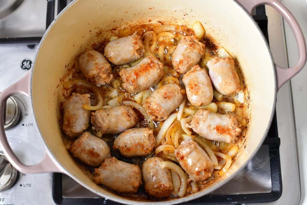 Sausage pieces and onion slices are being cooked in a large pot. 