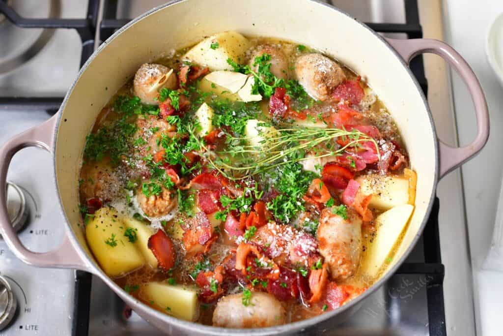 A large pot is filled with all of the ingredients for a Dublin Coddle and is garnished with fresh herbs.
