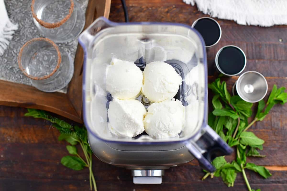 Four scoops of ice cream sit at the bottom of a blender.