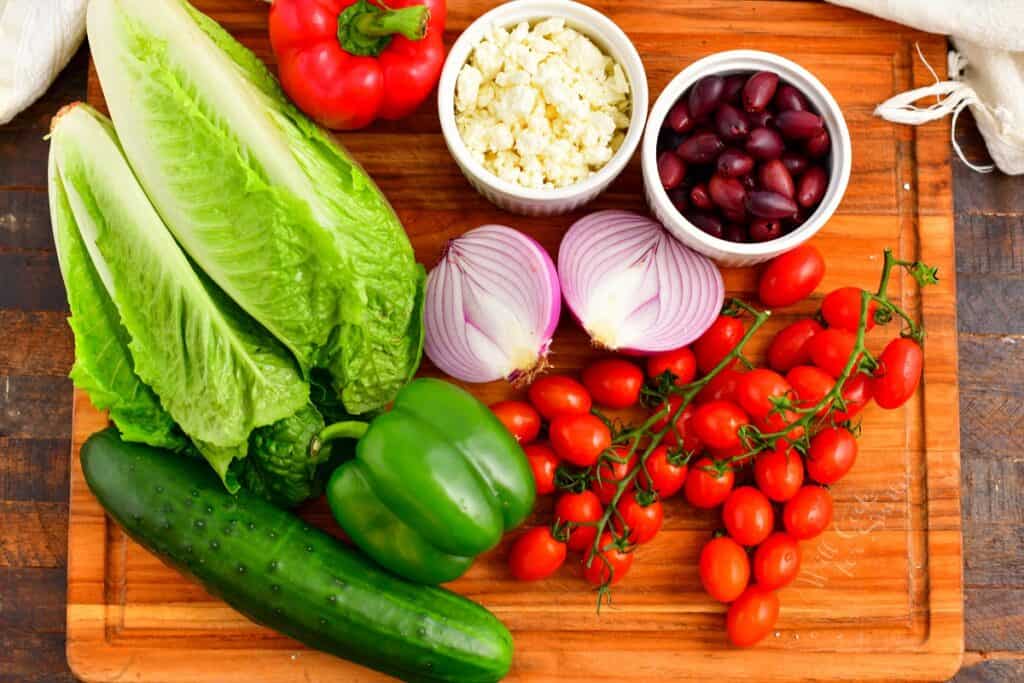 The ingredients for greek salad are placed on a wooden cutting board.