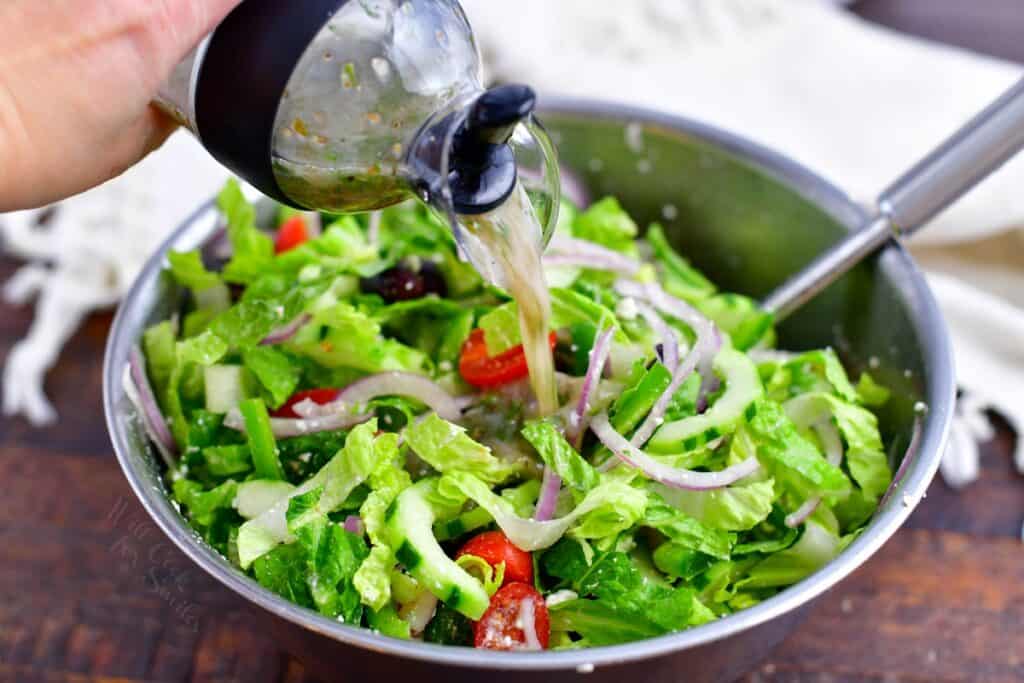 Dressing is being poured over a freshly tossed salad.