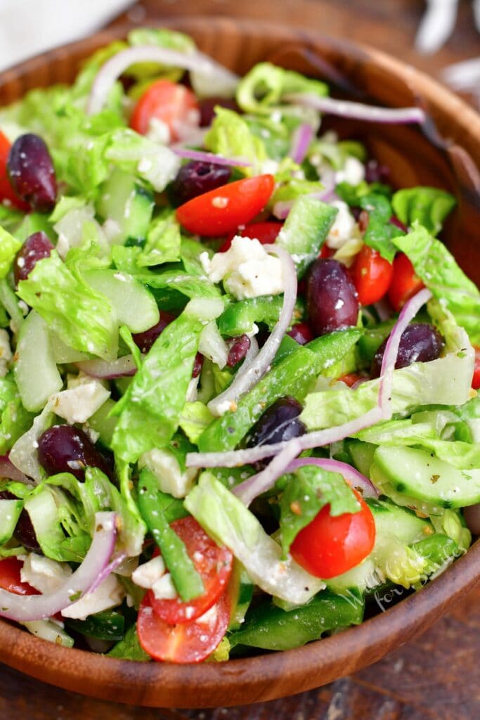 A close up shot reveals freshly chopped vegetables mixed together with dressing in a large bowl.