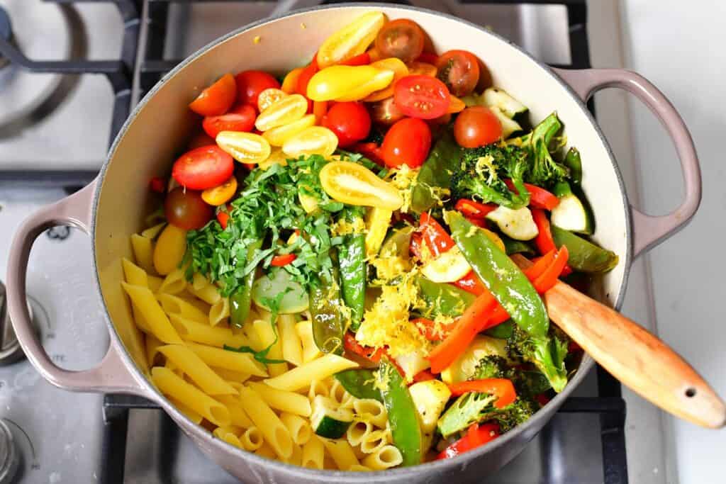 Pasta primavera is placed in a dutch oven on a stove top.