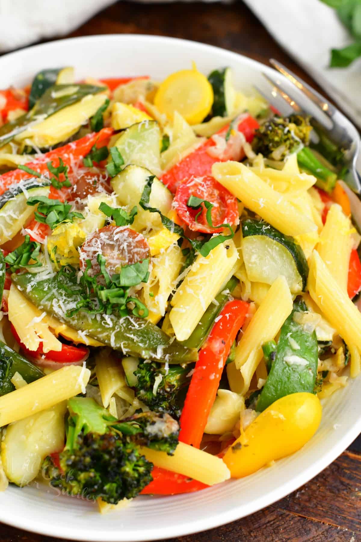 A white plate contains a large portion of pasta primavera. 