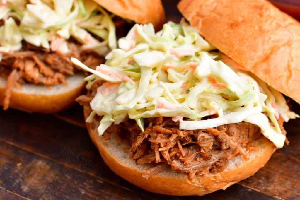 Coleslaw is sitting on a freshly made pulled pork sandwich. 