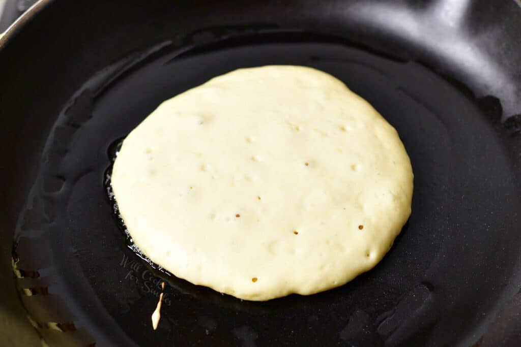 A pancake has bubbles forming in the batter, showing it's ready to be flipped in the black skillet.