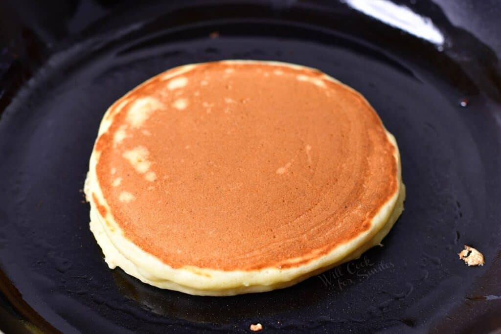 A ricotta pancake has been flipped in a black skillet.