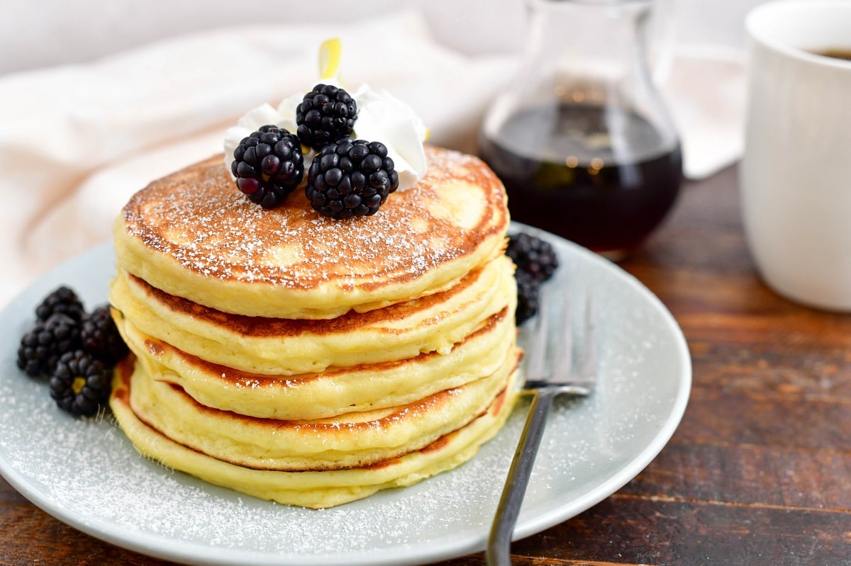 A stack of pancakes is topped with blackberries on a white plate.