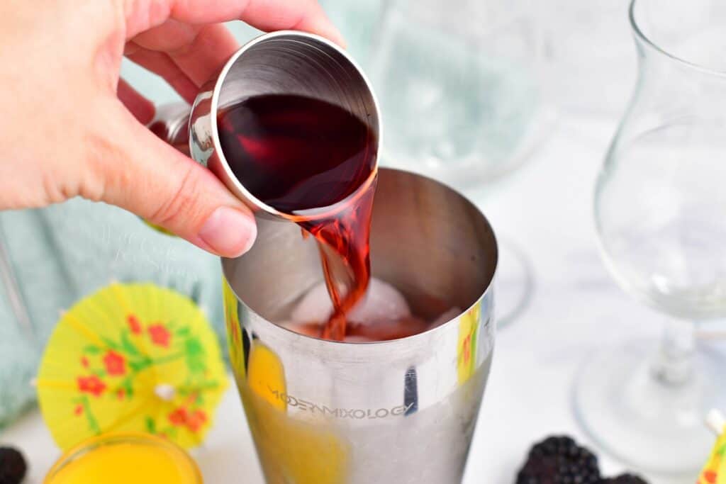 Dark rum is being poured into a cocktail shaker. 