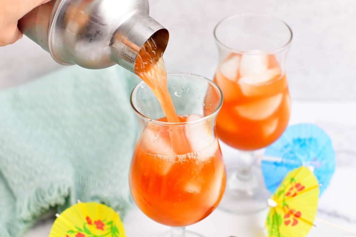 Rum runner cocktail is being poured from a cocktail shaker into a hurricane glass.