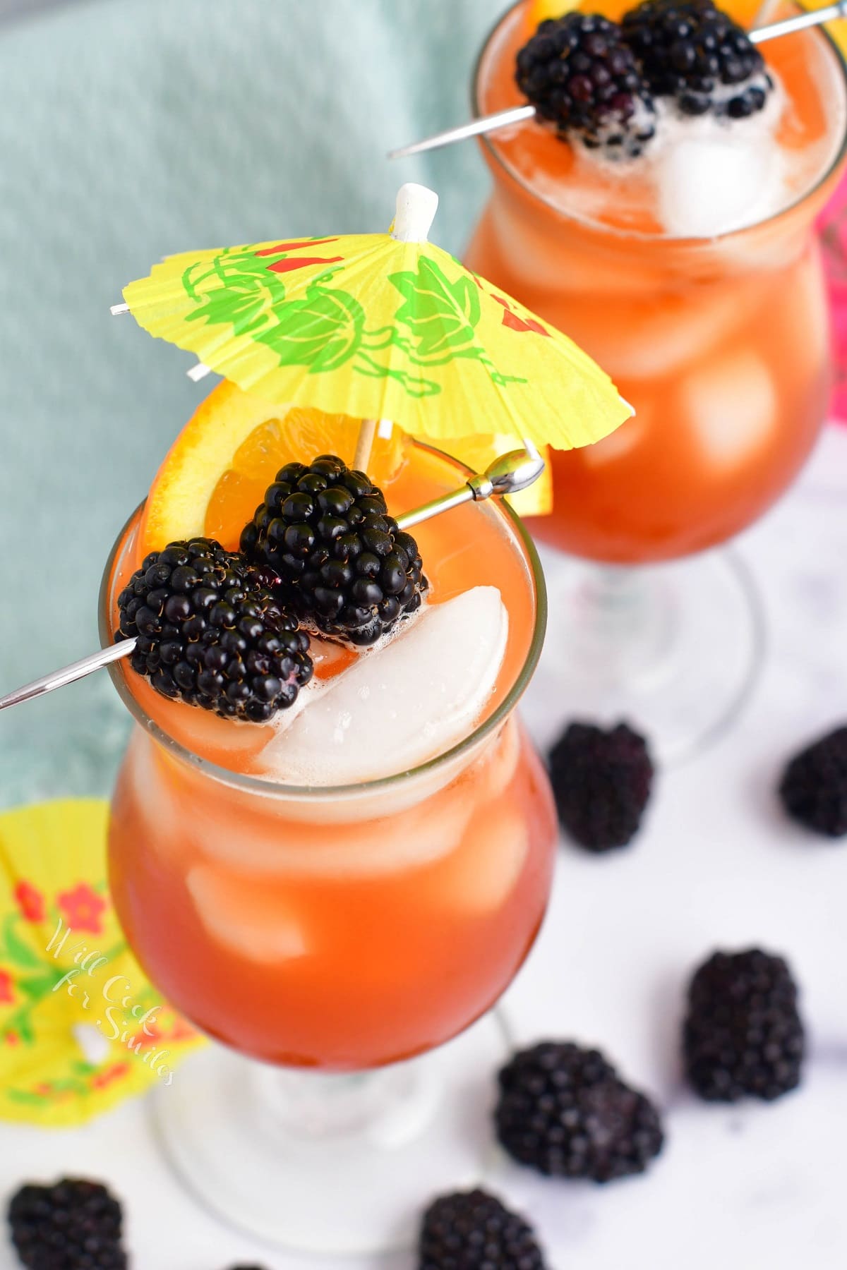 Two rum runners are in cocktail glasses and garnished with mini umbrellas and blackberries.