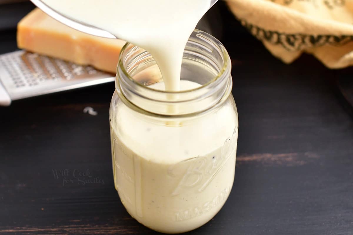 pouring alfredo sauce into the mason jar.