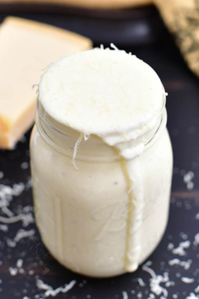 closeup of a glass jar filled with creamy sauce all the way to the top and dripping