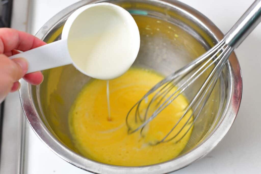A whisk is placed in a bowl full of yellow liquid.