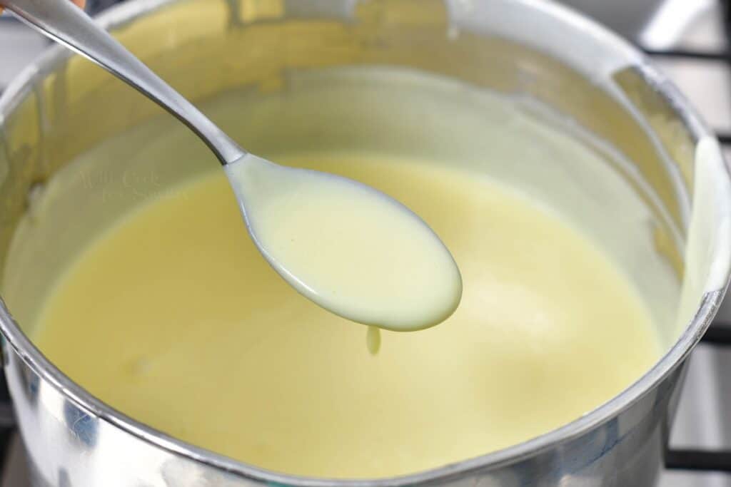 A spoon is holding a small portion of white liquid above a pot.