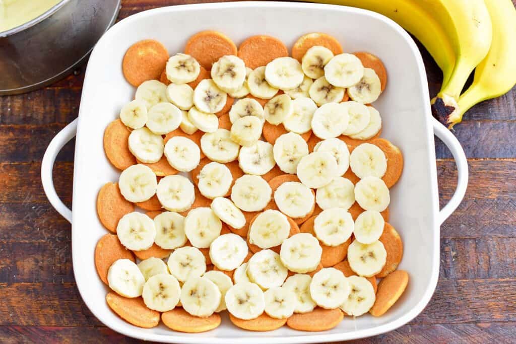 Nilla wafers and bananas are lining the bottom of a white dish.