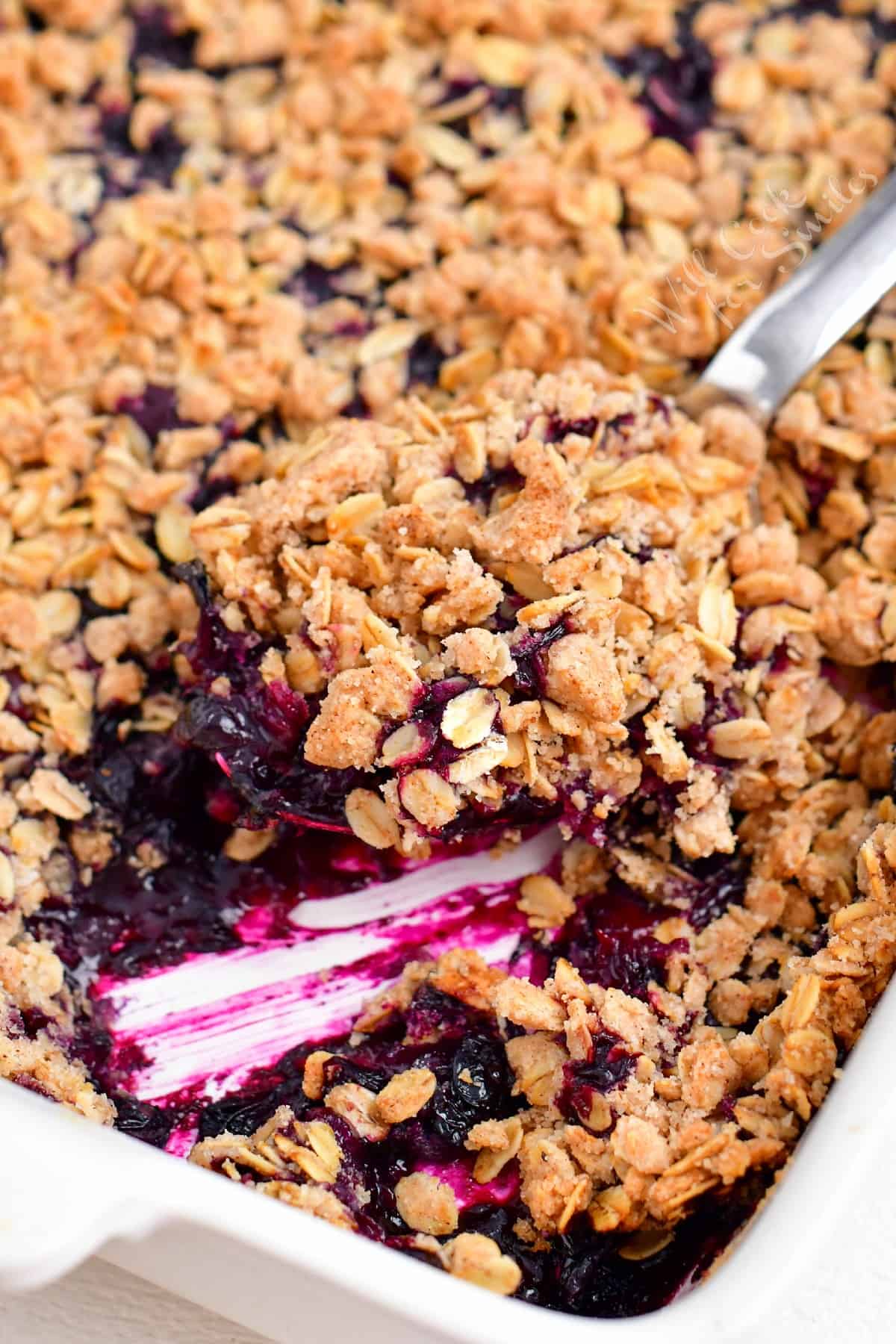 A scoop of blueberry crisp is being lifted from the casserole dish.