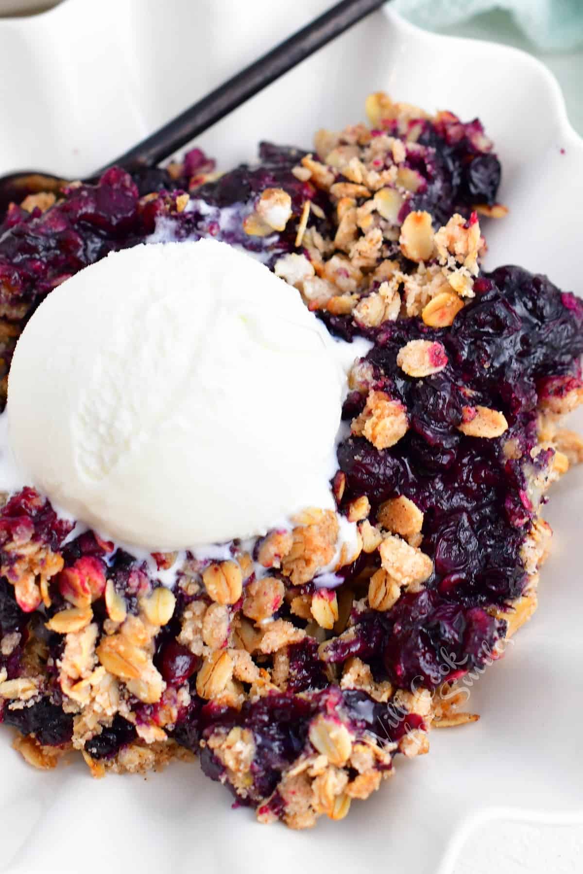 A scoop of vanilla ice cream sits atop a big bowl of blueberry crisp.