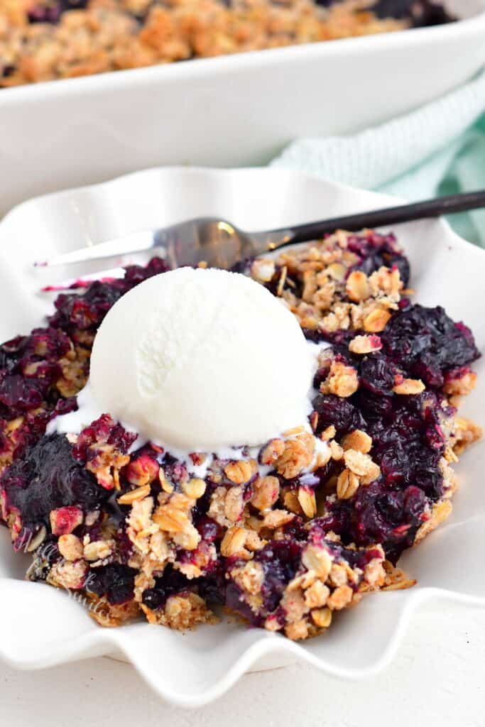 A fork is placed in a bowl with vanilla ice cream and blueberry crisp