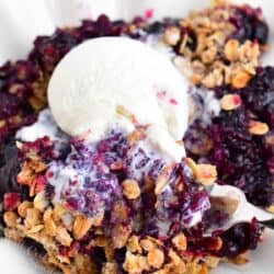 Ice cream is melting into a warm serving of blueberry crisp.