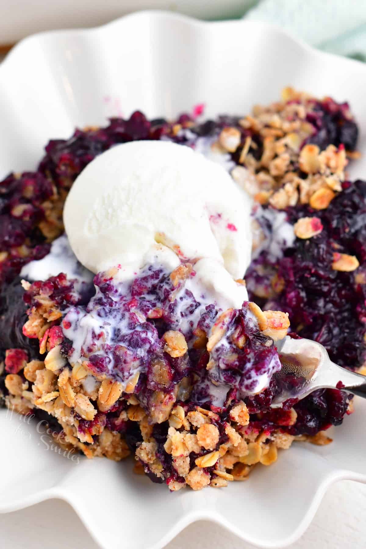 Ice cream is melting into a warm serving of blueberry crisp.