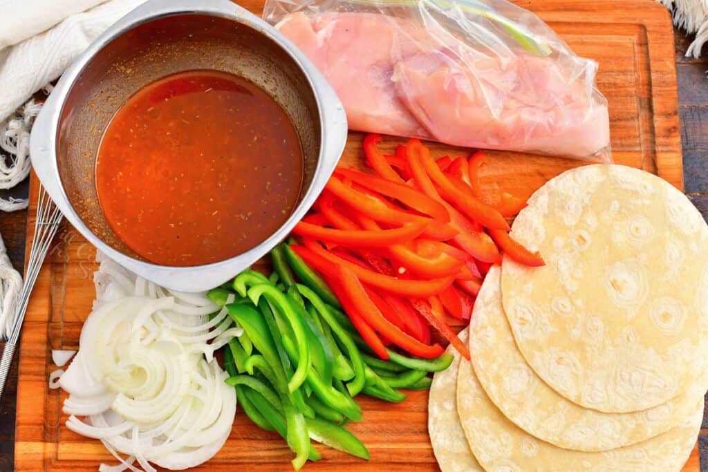 The ingredients for chicken fajitas are spread out on a wooden cutting board.