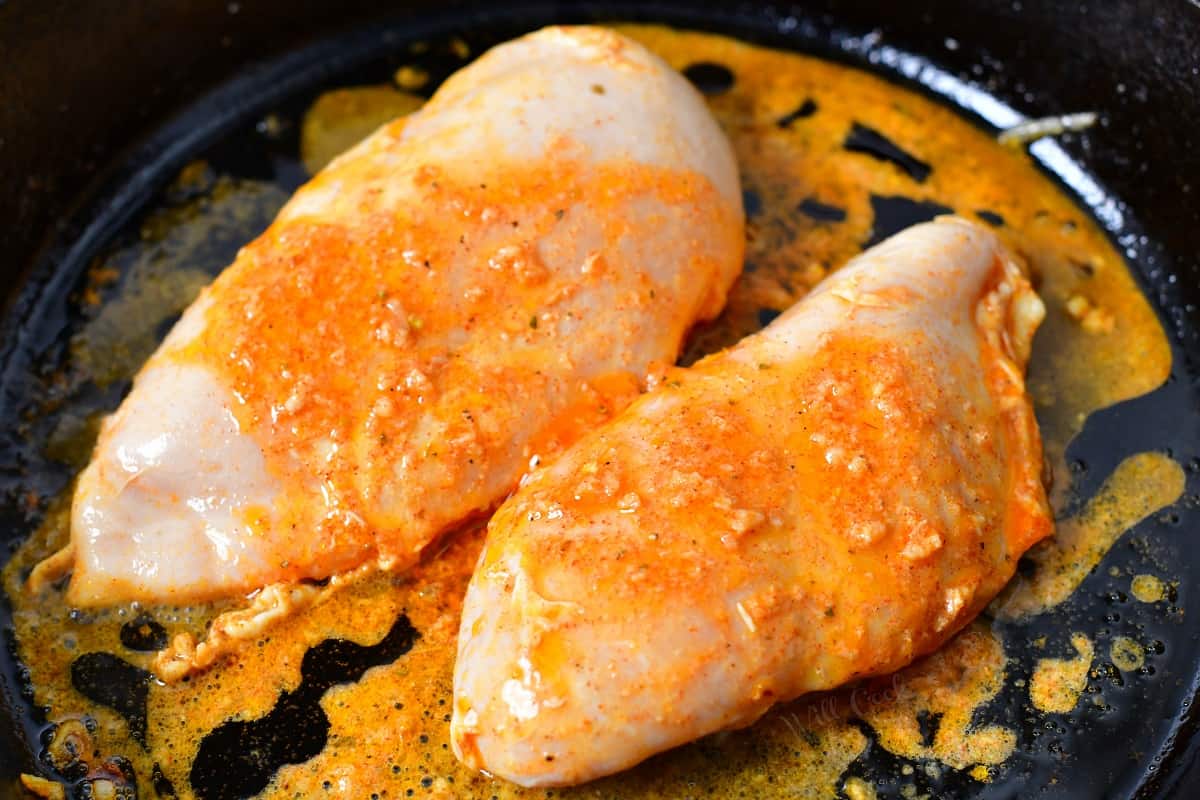 Uncooked chicken is doused with marinade in a black skillet.