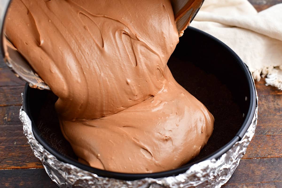 Cheesecake filling is being poured into a prepared baking dish. 