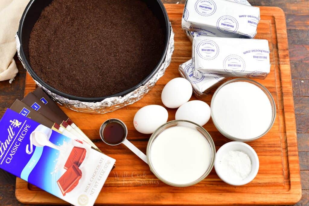 The ingredients for chocolate cheesecake are presented on a wooden surface. 