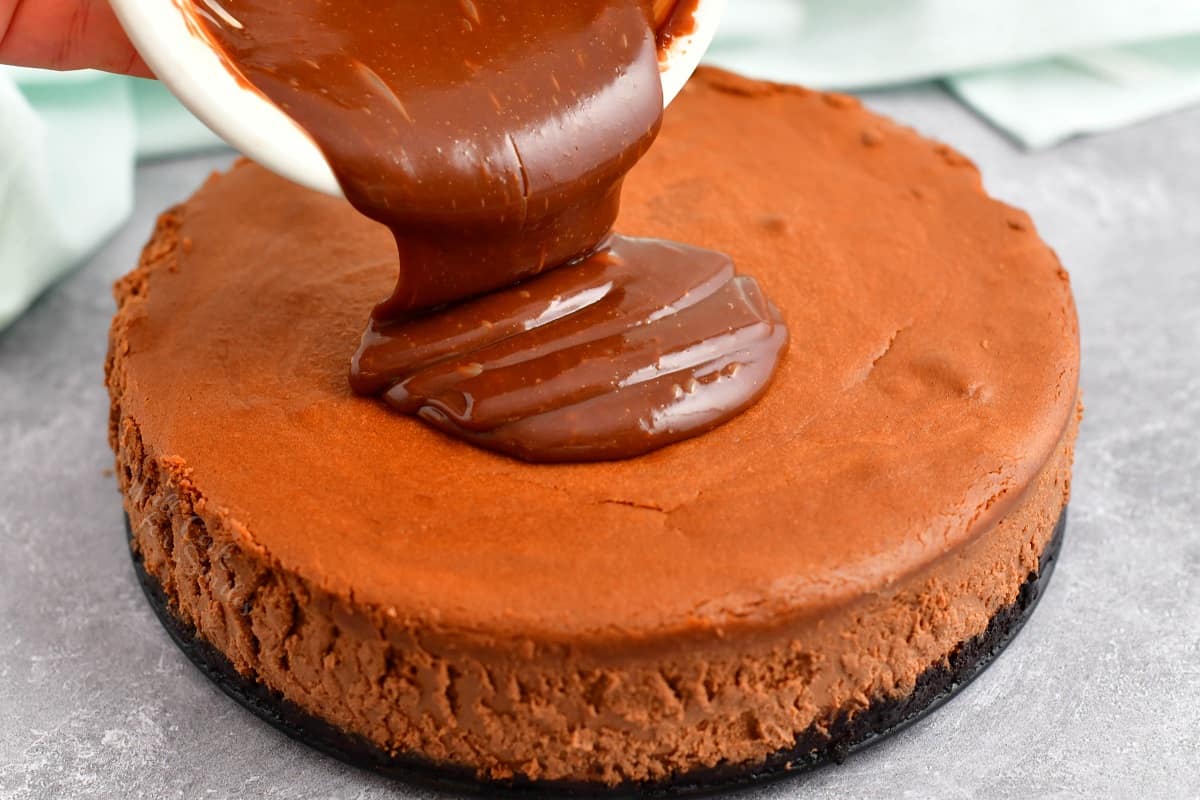 Chocolate ganache is being poured over a cheesecake.