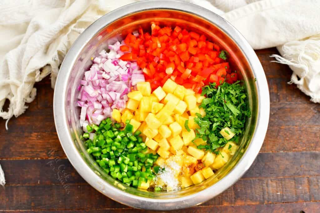 The ingredients for fresh pineapple salsa are placed in a large silver bowl. 