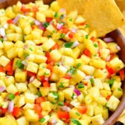 Chips are placed on the side of a bowl filled with pineapple salsa.