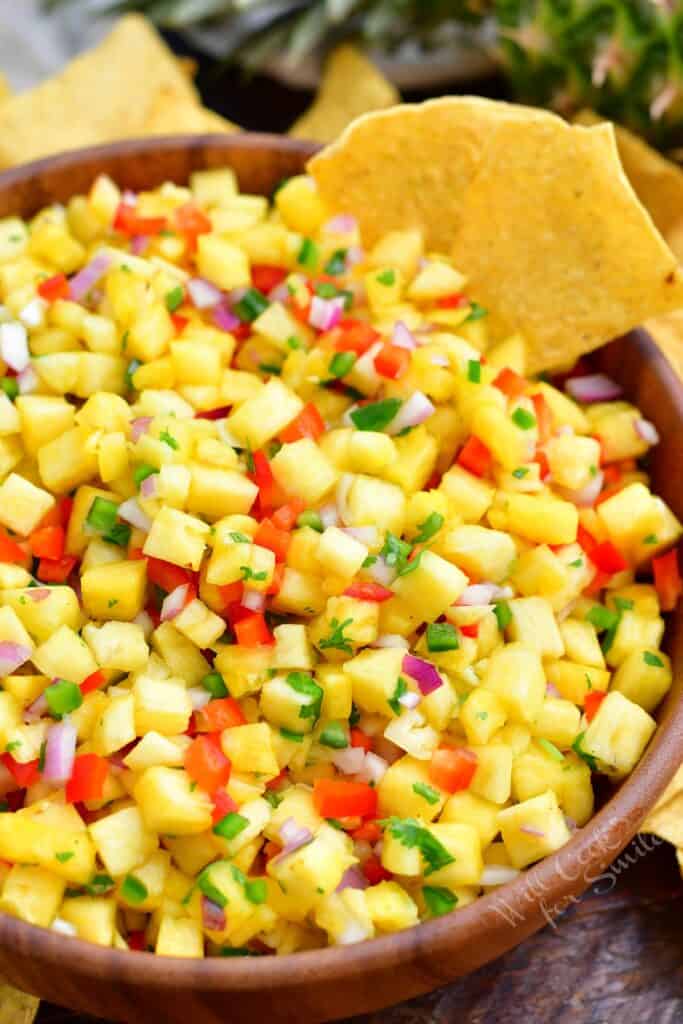 Chips are placed on the side of a bowl filled with pineapple salsa.