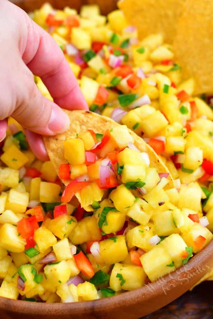 A chip is dipped into pineapple salsa.