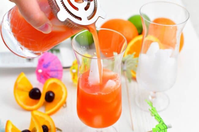 Punch is being poured from a cocktail strainer into a glass over ice.