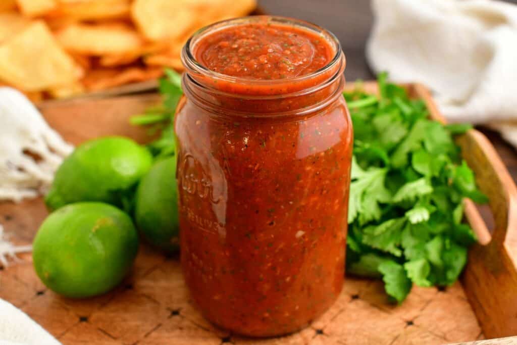 Salsa is in a jar next to limes and cilantro.