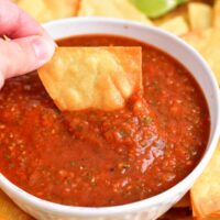 A chip is being dipped into red salsa.