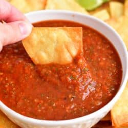 A chip is being dipped into red salsa.