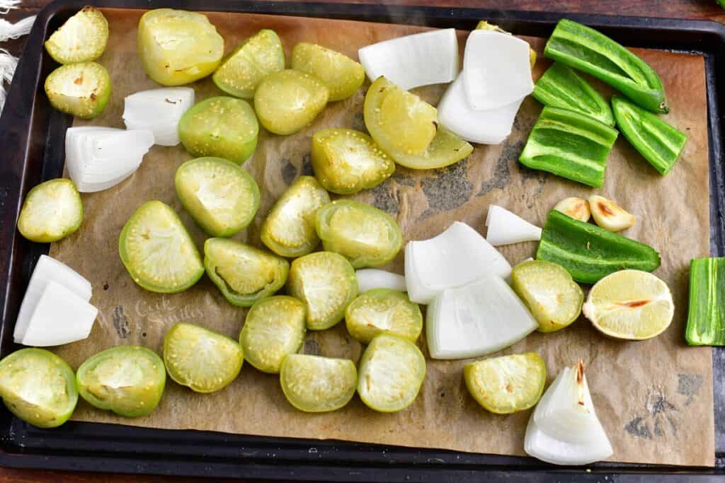 The ingredients for salsa verde are spread out on a baking sheet and have been cooked.