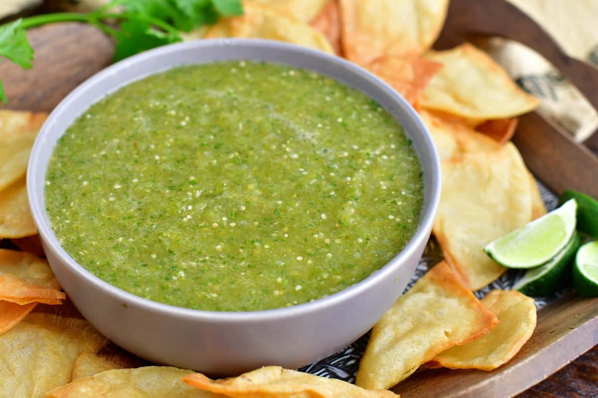 A bowl of green salsa is surrounded by chips.