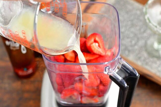 Liquid is being poured into a blender of strawberries. 