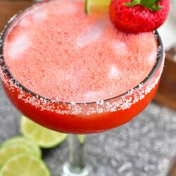 A strawberry and lime slice garnish a glass of strawberry margarita.