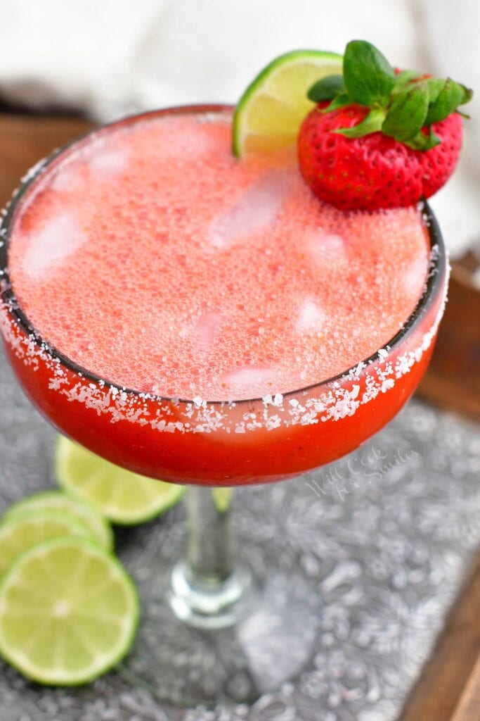 A strawberry and lime slice garnish a glass of strawberry margarita. 