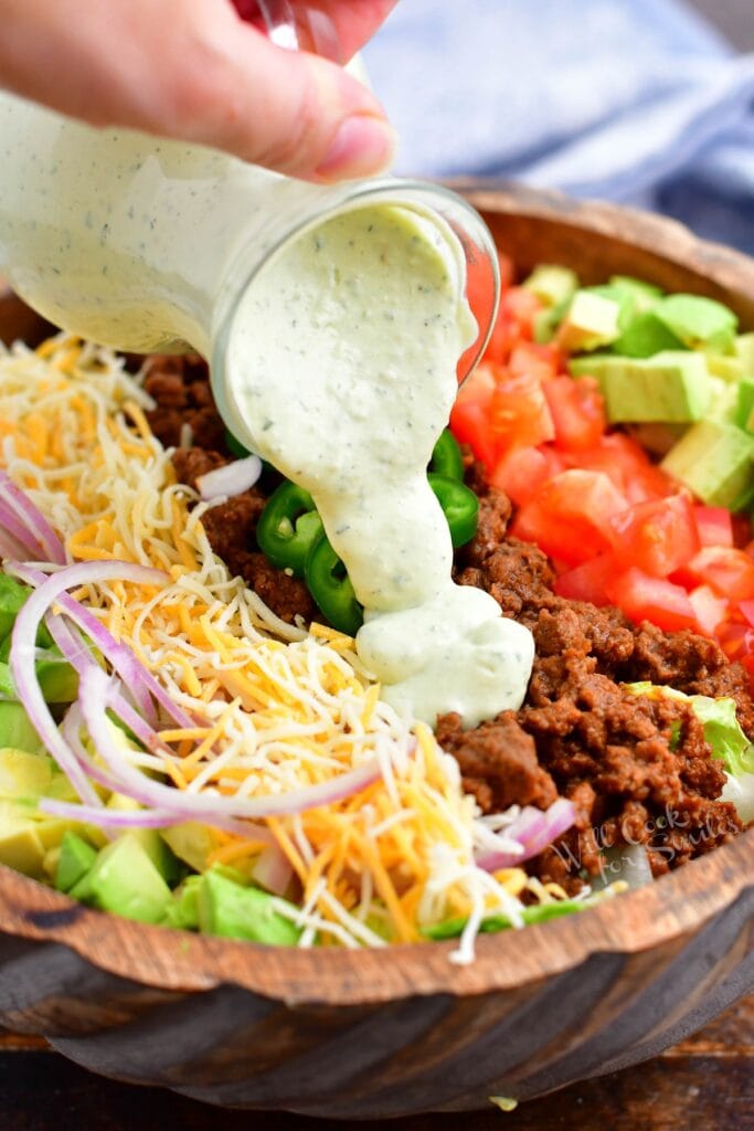 Avocado dressing is being poured on top of a salad.