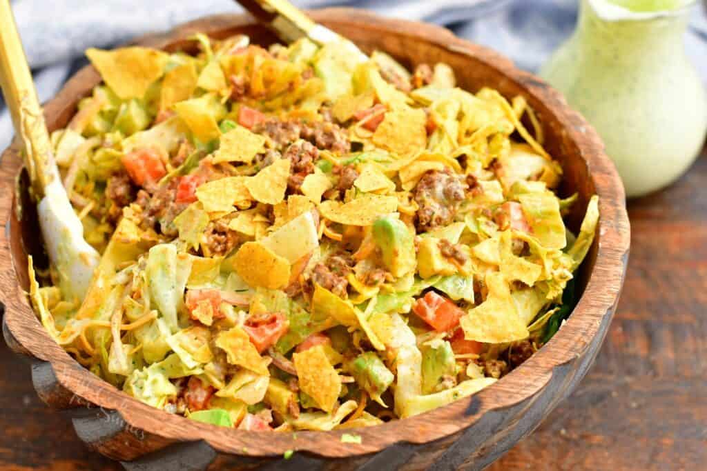 A taco salad is tossed in a wooden bowl. 