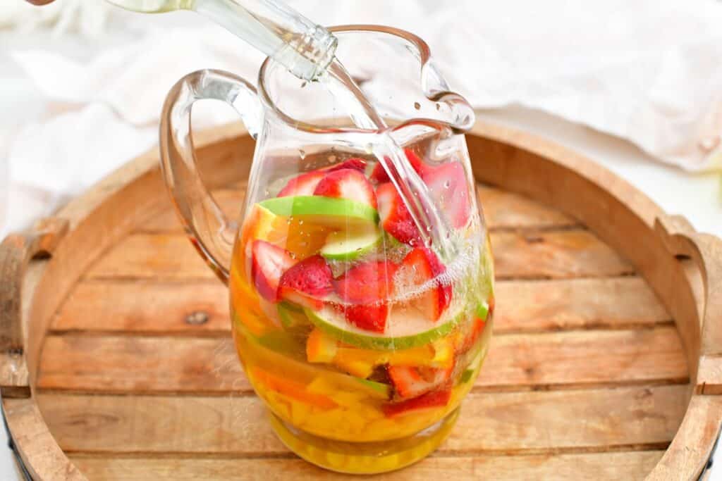 Clear liquid is being added to a pitcher of fruit. 