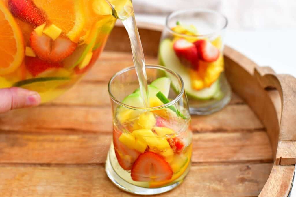 A pitcher is pouring sangria into a small, round glass.