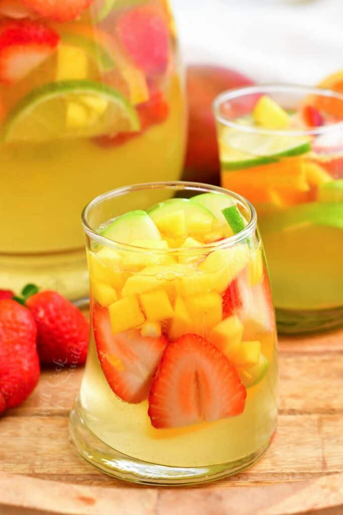 Two glasses of white sangria are placed next to a full pitcher. 