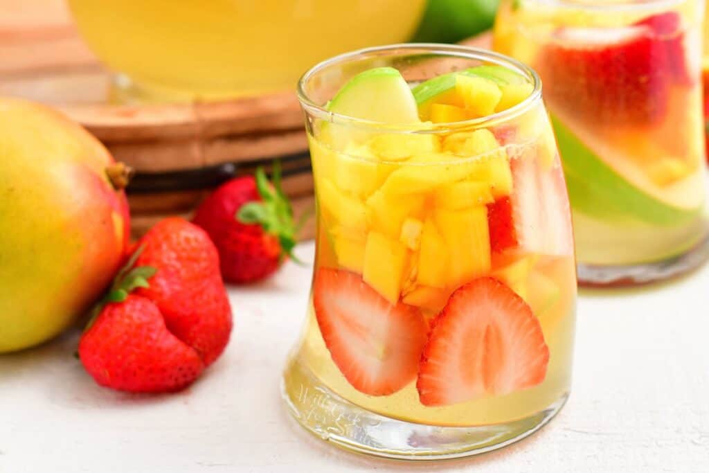 Strawberries and mangoes are in a glass willed with sangria. 